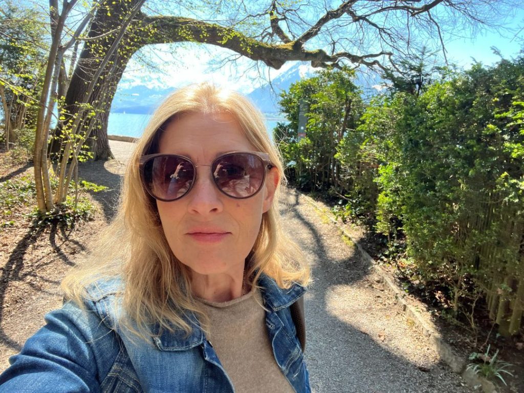 Woman standing at the start of a path in a sunny outdoor setting, looking calm and decided.