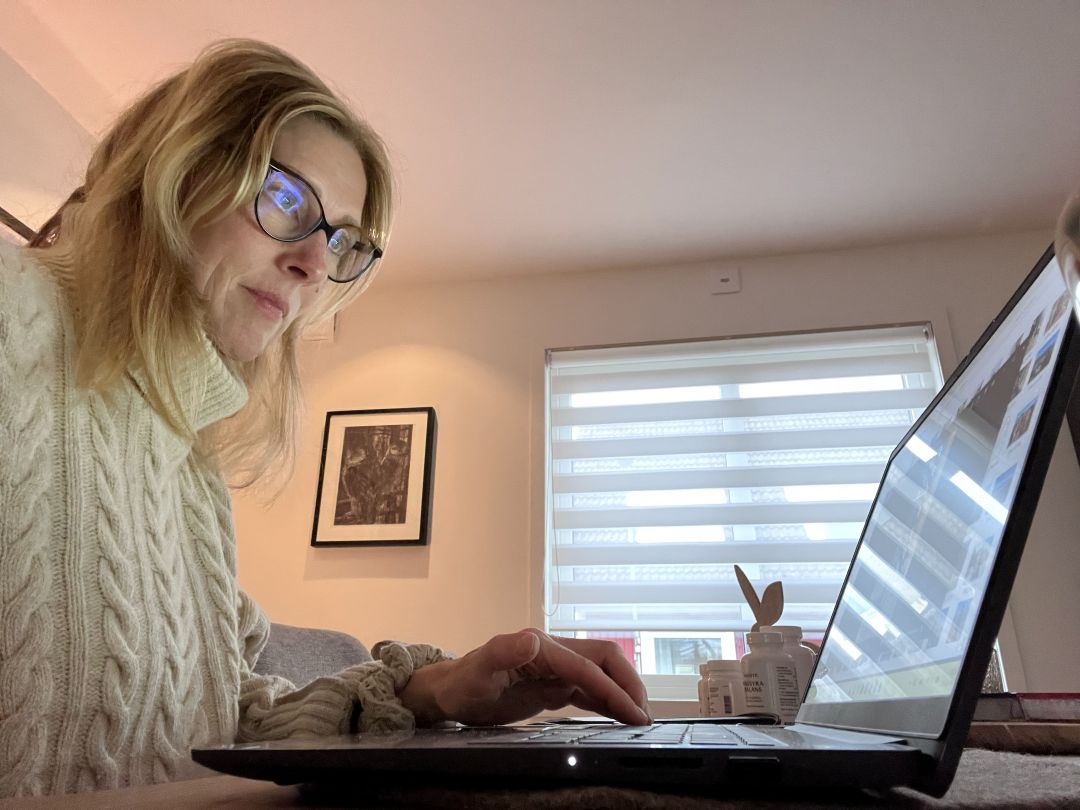 Woman in her 50s working on a laptop at home, focused and relaxed in a natural light setting.
