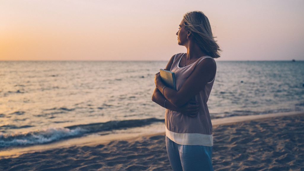 Woman standing on a beach, reflecting on life and new possibilities as retirement approaches.