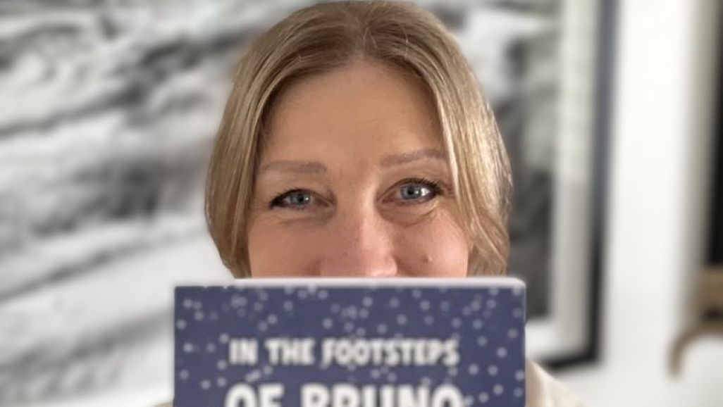 Smiling author with eyes showing above their debut book, In the Footsteps of Bruno